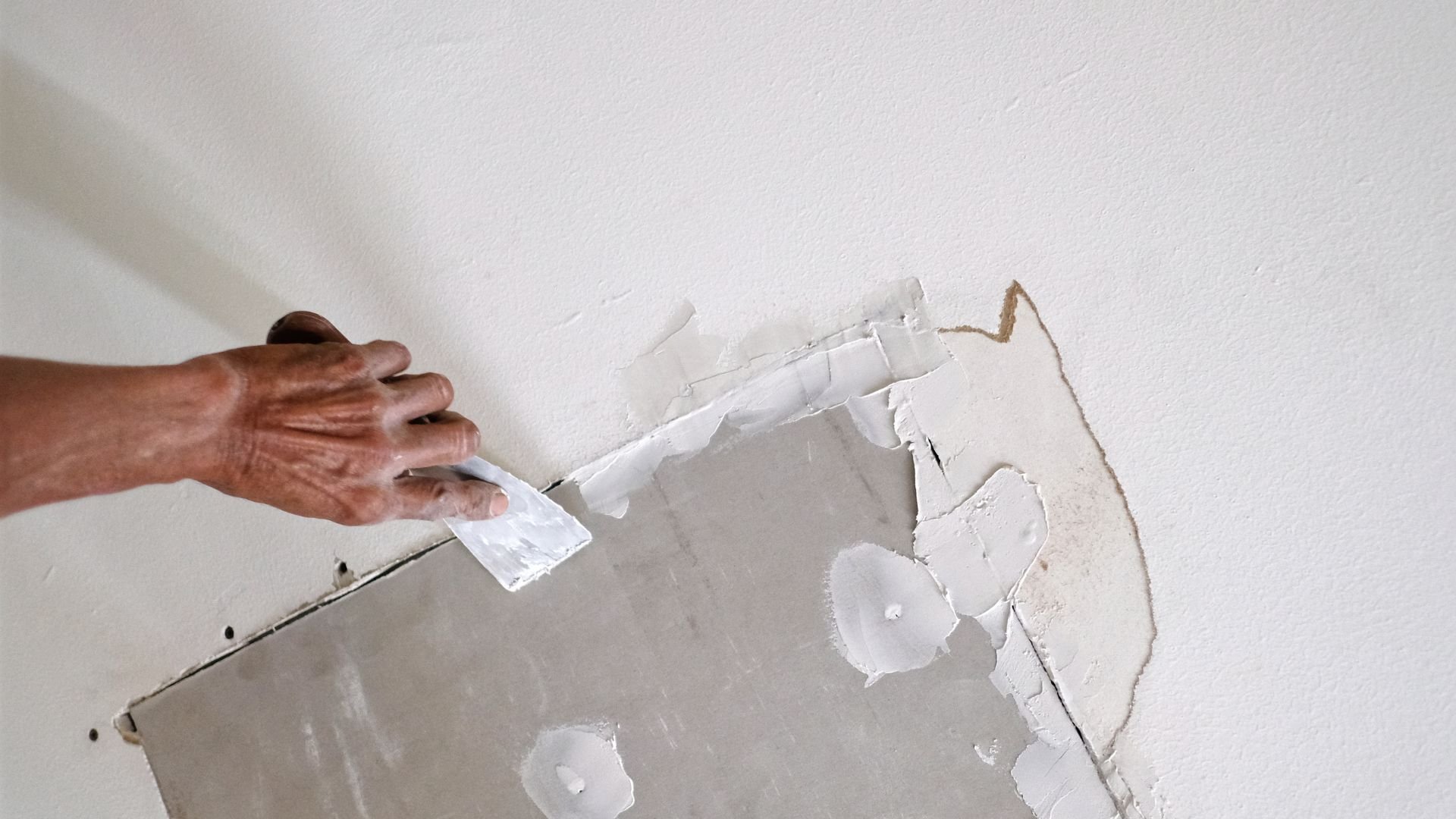 Hand scraping damaged wall with putty knife during home repair