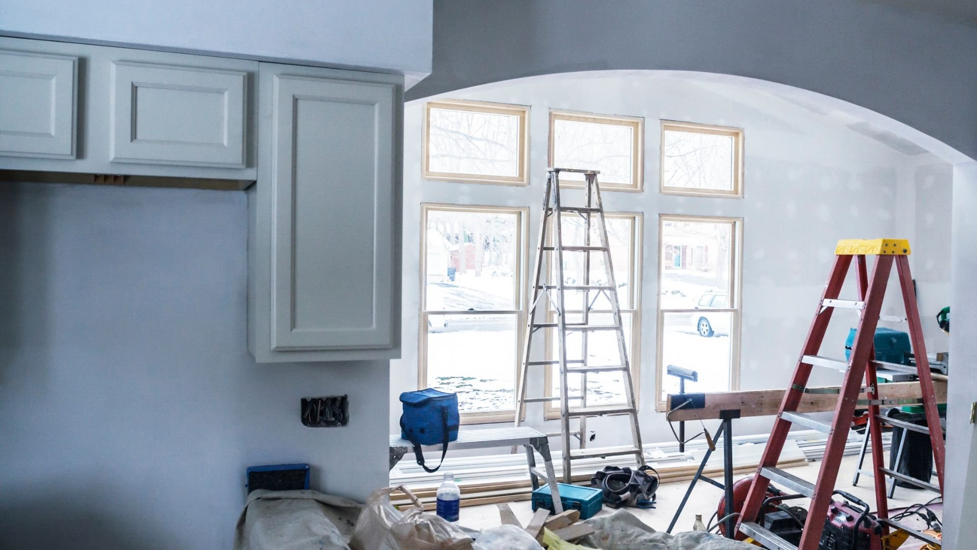 Home renovation in progress with ladders, tools, and windows