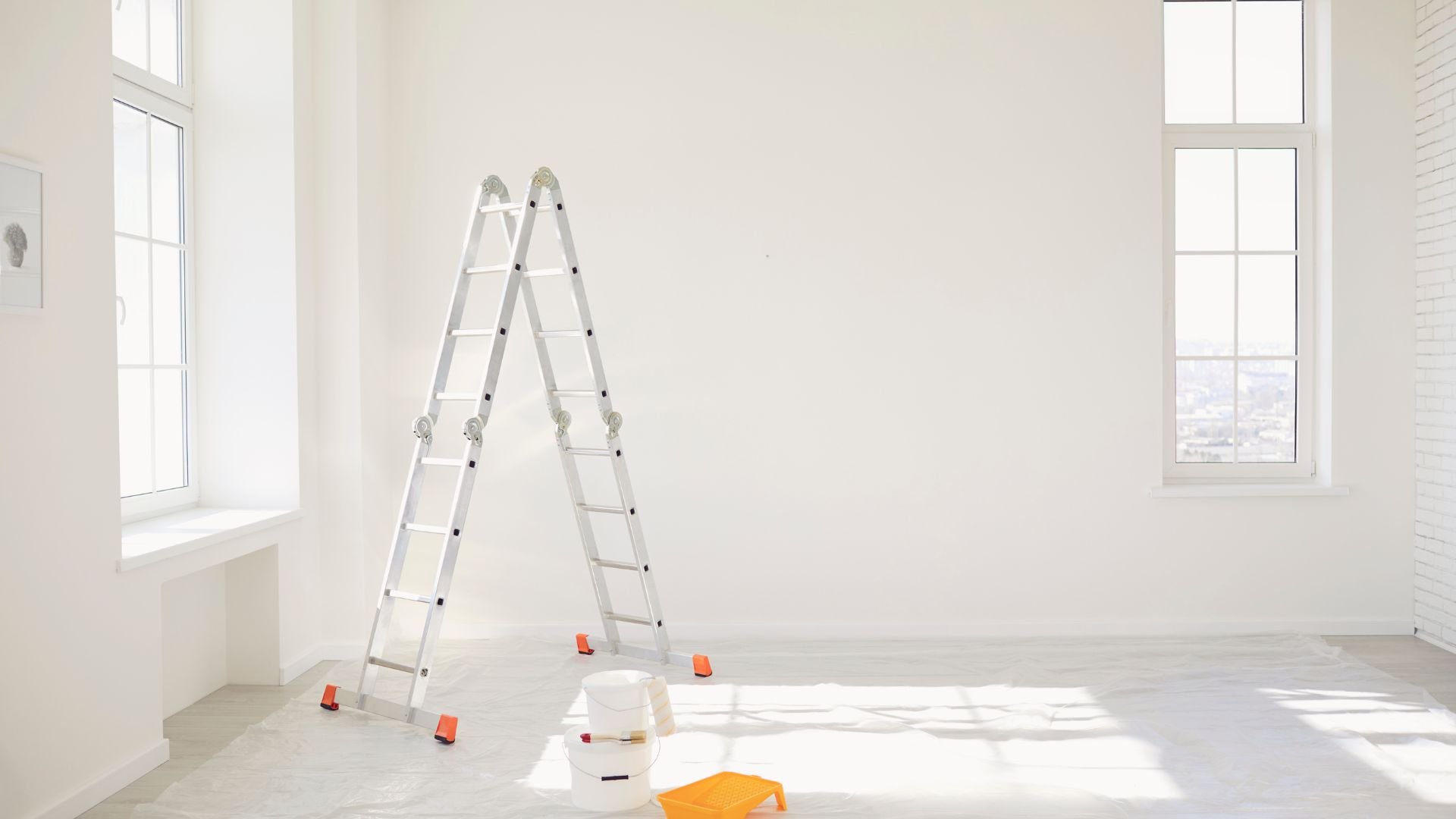 White room with ladder, paint bucket, and orange tools for renovation