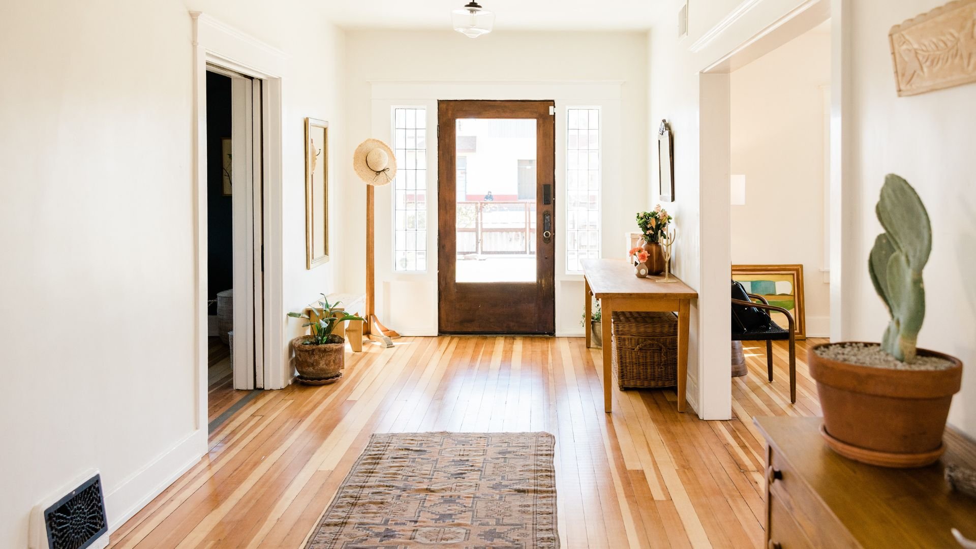 Bright entryway with wooden floor, plants, hat, and glass front door
